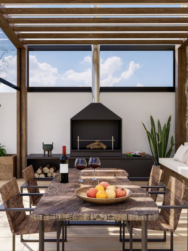 New-Project-2026-04-06T084721.516-opt Outdoor dining area under a wooden pergola with a built-in grill; a rustic table holds wine, two glasses, and a bowl of fruit, with sky visible in the background and potted plants nearby.